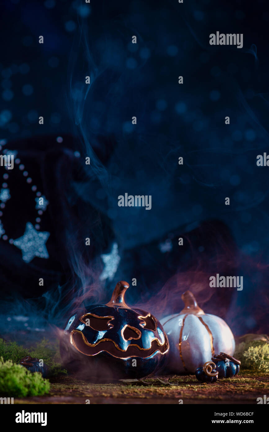 Calabazas de cerámica con asistente sombrero puntiagudo, musgo y las hojas caídas sobre un fondo oscuro con espacio de copia. Halloween bodegón Foto de stock