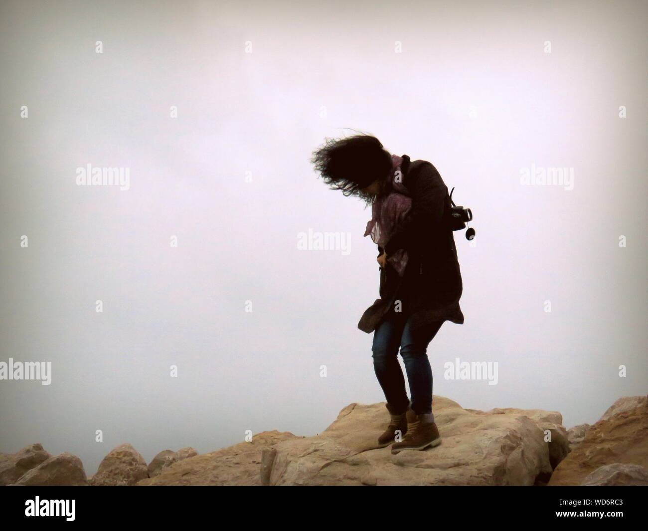 La longitud completa de la Mujer de pie sobre una roca contra el cielo durante el día ventoso Foto de stock