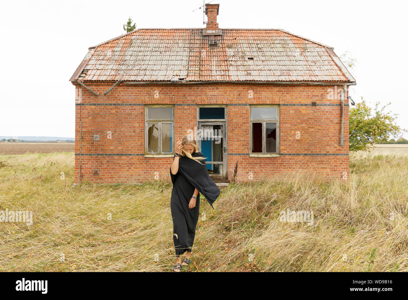 Mujer vistiendo negro por casa abandonada Foto de stock