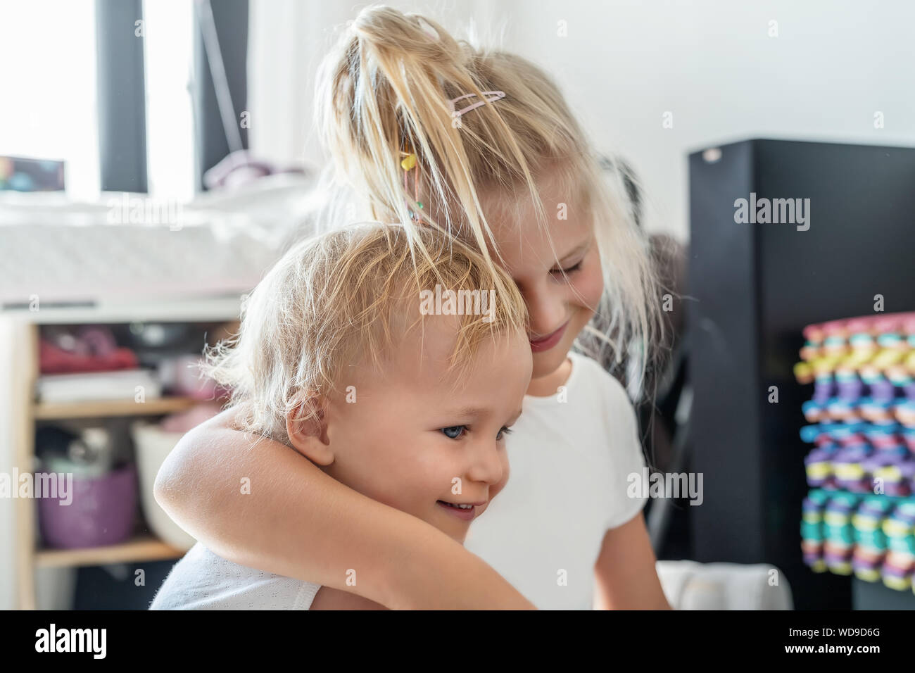 Cute adorable rubia caucaian hermanita abrazando a su hijo hermano.Par de hermano alegre jugando indoor. Linda chica y baby boy disfrutar Foto de stock
