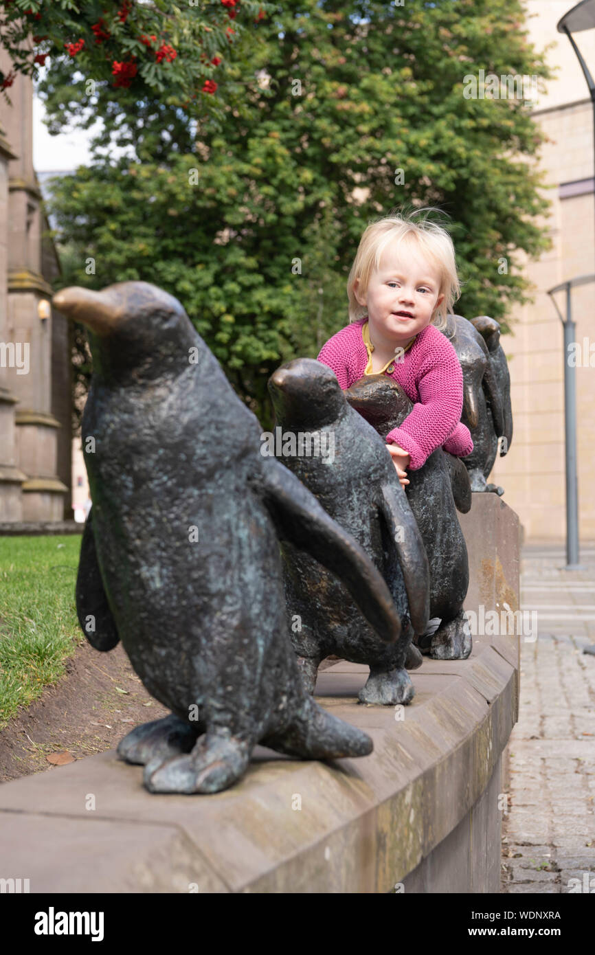 Un niño abraza a uno de los cinco pingüinos en la Escultura por Angela Hunter, cerca del centro comercial Overgate en Dundee Foto de stock