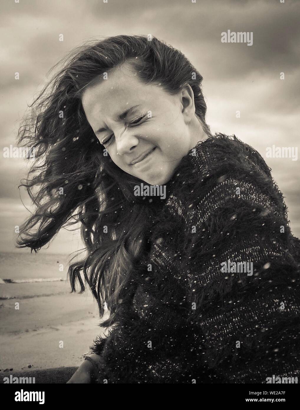 Mujer joven con los ojos cerrados en la playa durante el viento Foto de stock