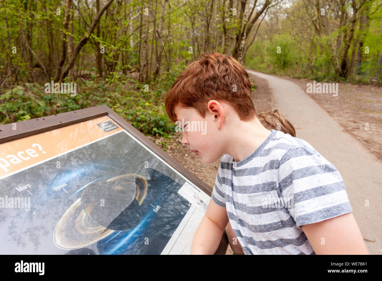 Un chico Mirando y leyendo una junta sobre el sistema solar en Ruislip Lido, Greater London Foto de stock