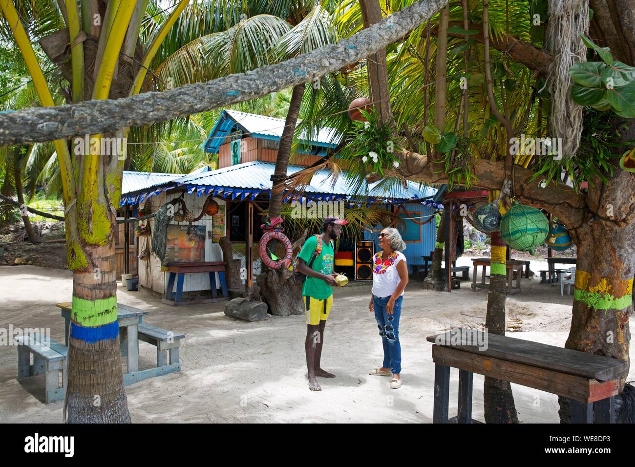 Colombia, la isla de Providencia, Colombia pareja conversando sobre la arena de Rolland's bar, un bar oculto bajo la vegetación tropical en la playa de Manzanillo Foto de stock