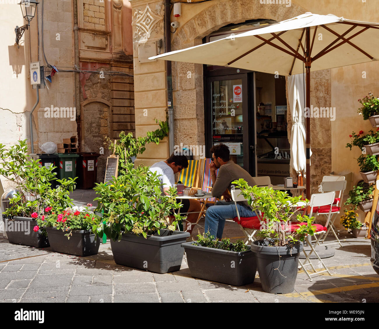 Mesas en el exterior, sombrilla, macetas con plantas, 2 hombres sentados,  personas, restaurante, escenas urbanas, Europa; Ortigia Siracusa Sicilia;;;  Italia; muelle Fotografía de stock - Alamy