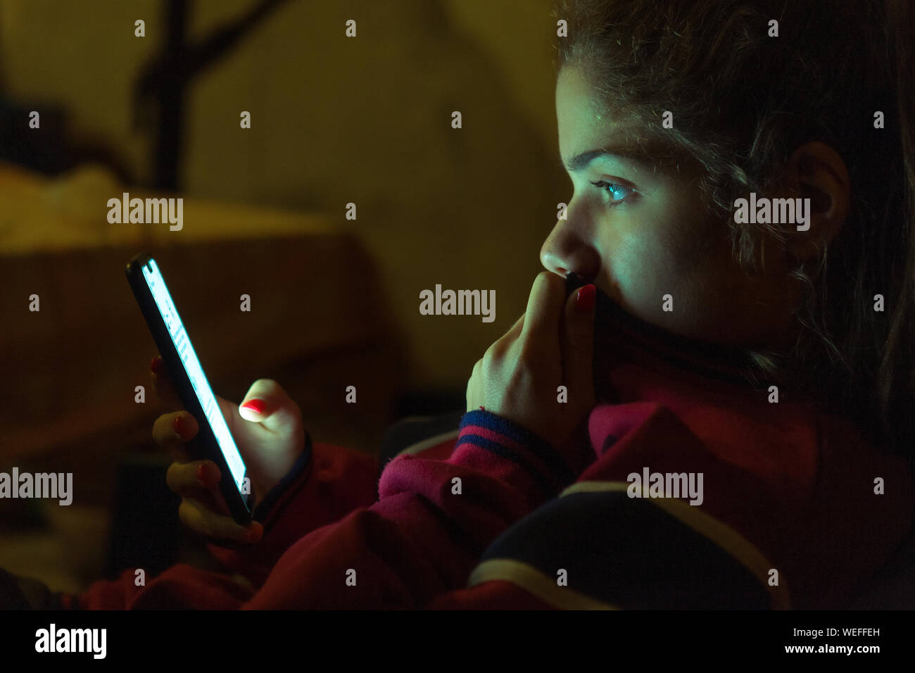 Luz del teléfono móvil iluminando el rostro de una adolescente navegando Foto de stock