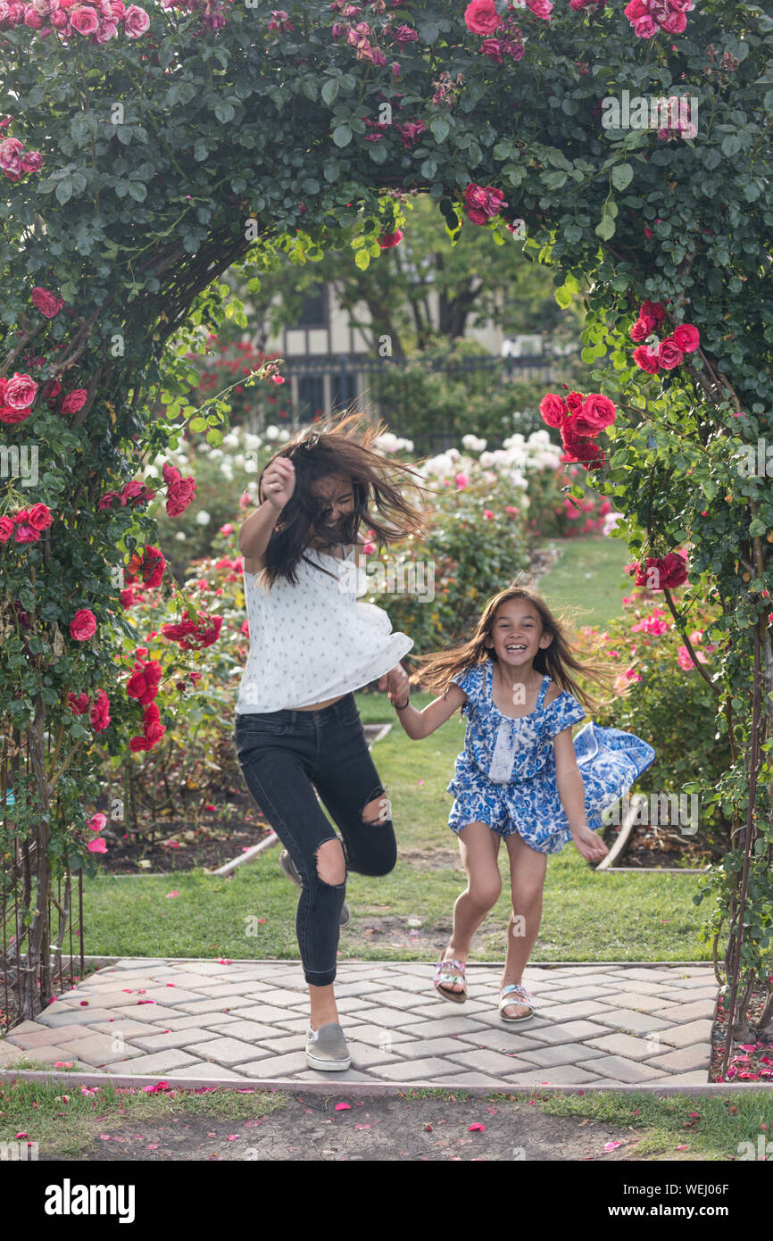Adolescente Aisan correr, saltar y reír con preadolescentes hermana en Rose Garden, San Jose, California Foto de stock