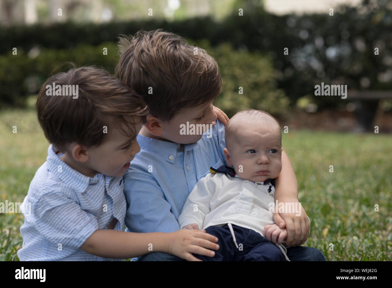 Dos niños, de 4 años y 2 año de edad, sosteniendo su hermanito en un parque Foto de stock