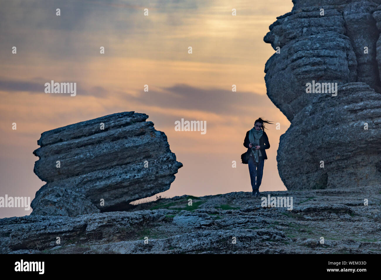 Mujer de pie con cámara por formaciones de roca en El Torcal de Antequera contra el cielo nublado durante la puesta de sol Foto de stock