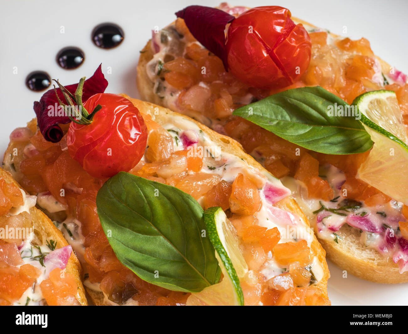 Bruschetta con queso crema y salazones de pescado cocido con tomate y albahaca Foto de stock