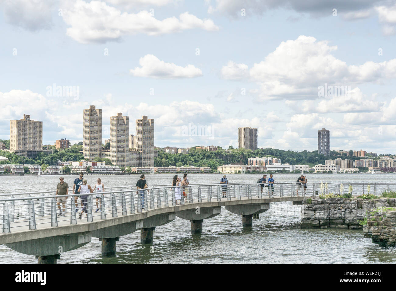 Multitud wpeople puente peatonal cruzando una pequeña entrada en Hudson River Park con amplias vistas del agua y variedad bajo & highrise alojamiento en Nueva Jersey Shore Foto de stock