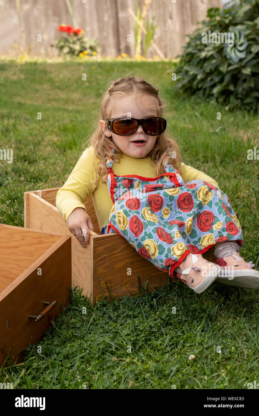 Lily modeling Grandma's gafas y delantal, sentada en un cajón vacío de ser descartado Foto de stock
