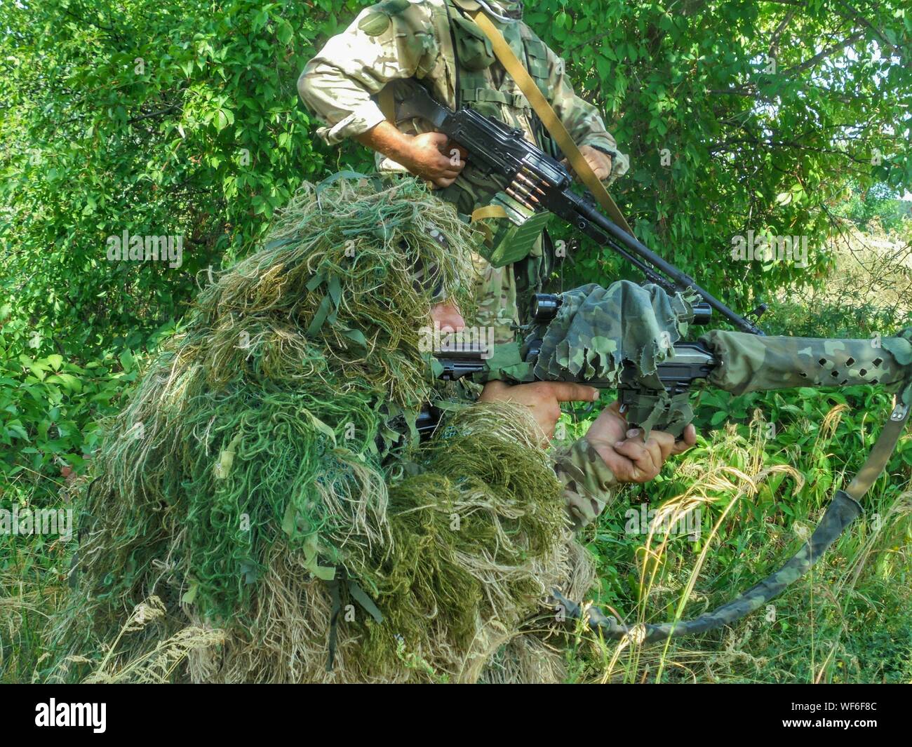 Vista lateral de los hombres con armas del ejército en medio del verde Foto de stock