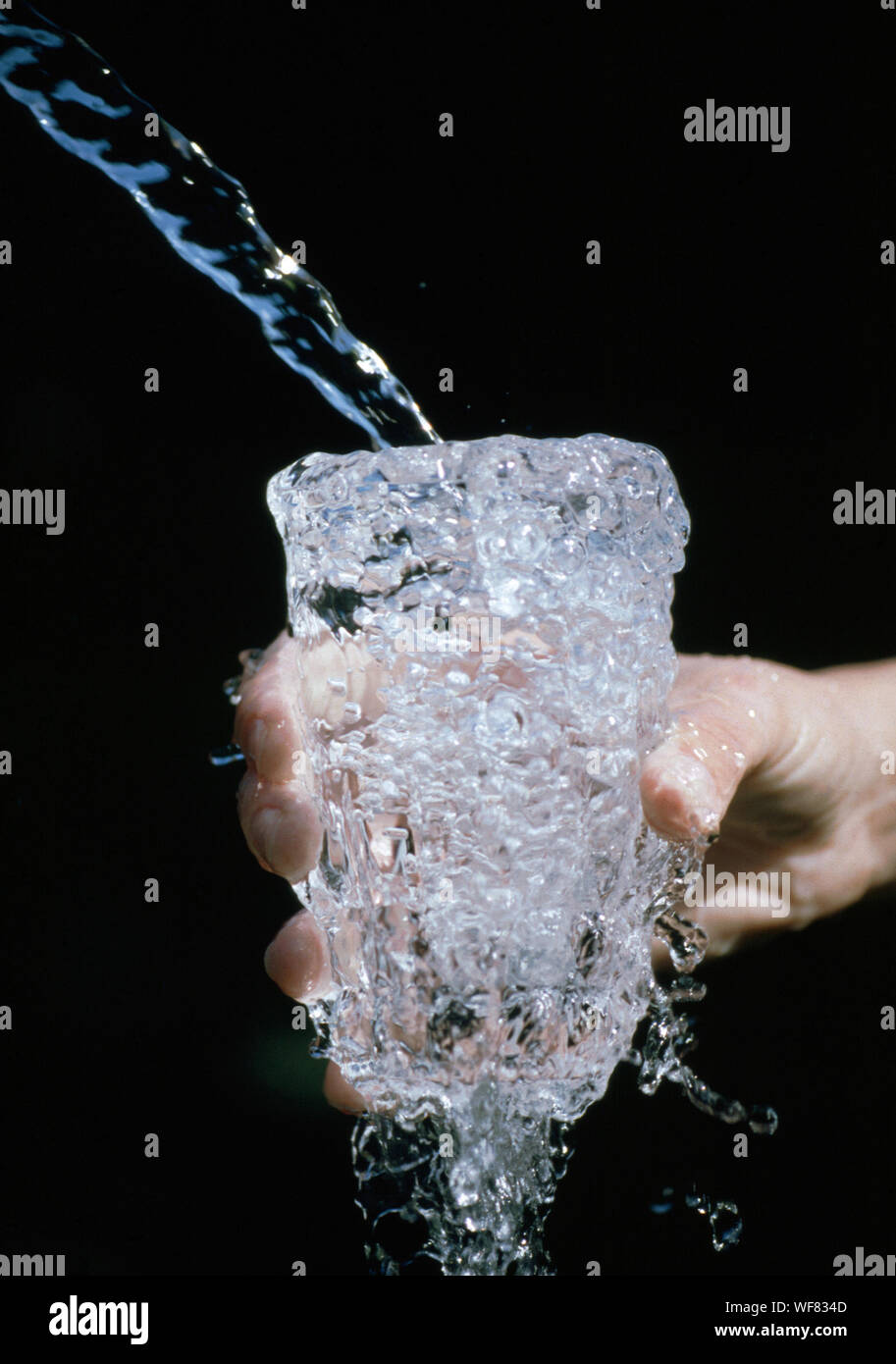 Mano sujetando recortadas rebosante vaso de agua contra el fondo negro  Fotografía de stock - Alamy
