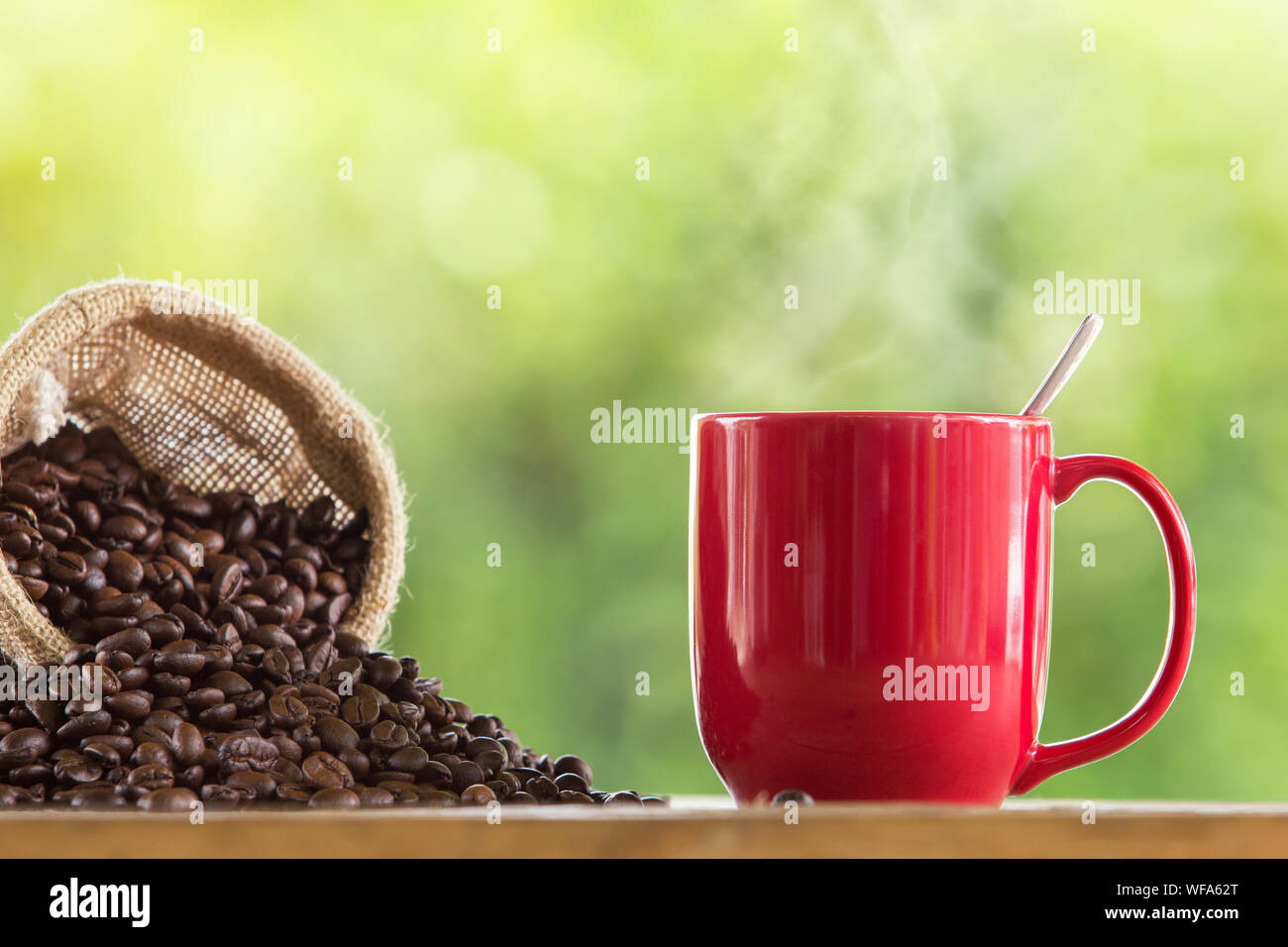 Los granos de café derramándose desde el saco por taza roja sobre la