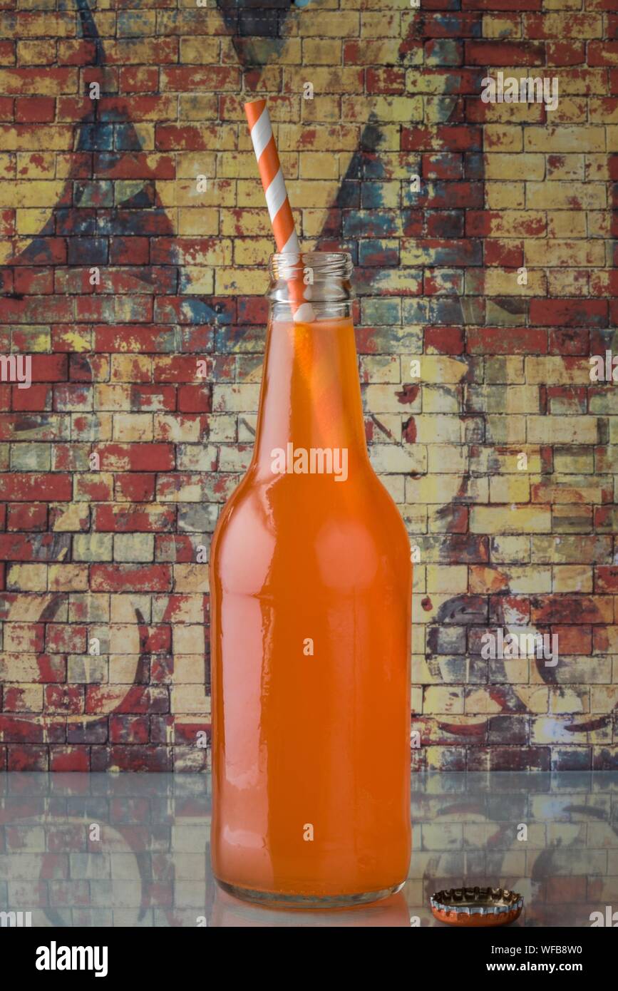 Botella de refresco de naranja con paja para beber en la mesa contra la pared de graffiti Foto de stock
