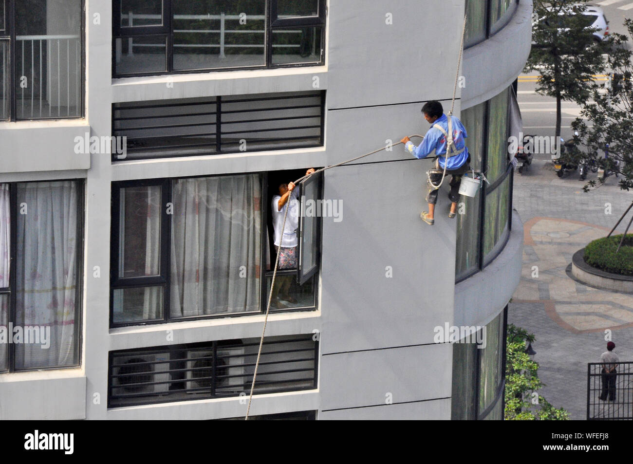 Un limpiador de ventanas para bloques de torre obtiene su cuerda enredada y un morador plana ayuda a cabo, Nantong China Foto de stock