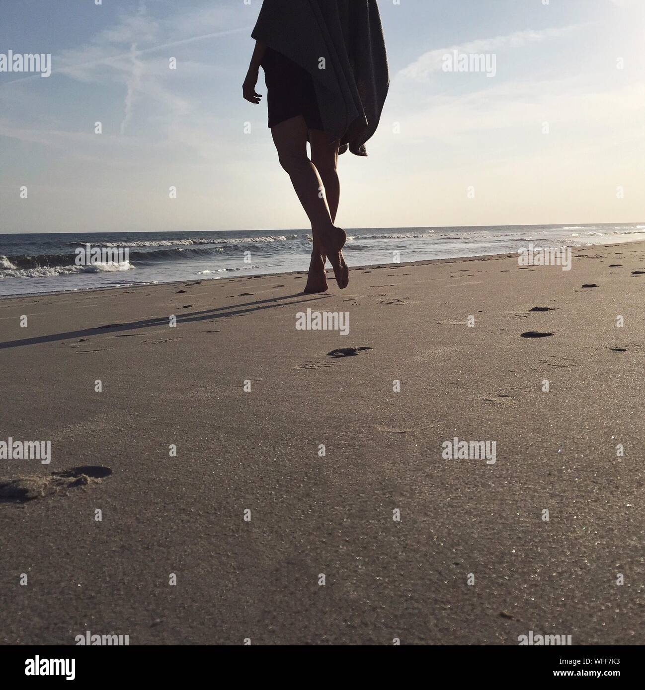 Bajo la sección de mujer y caminando en el Atlantic Beach contra el cielo Foto de stock