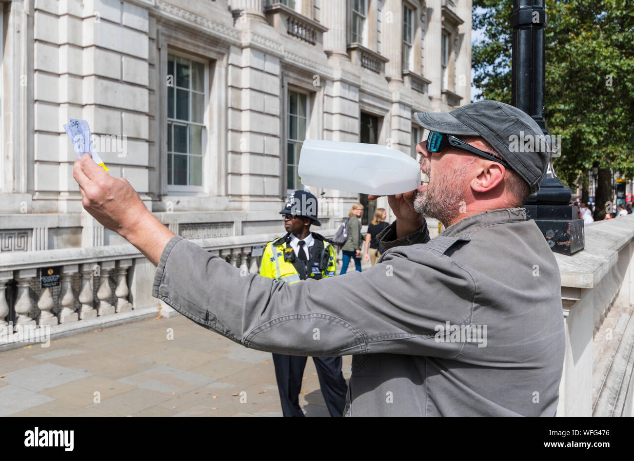 Manifestante solitario fuera de la Oficina del Gabinete en Whitehall en Londres gritando por megáfono casero a PM, con la policía mirando. La libertad de expresión en el Reino Unido. Foto de stock