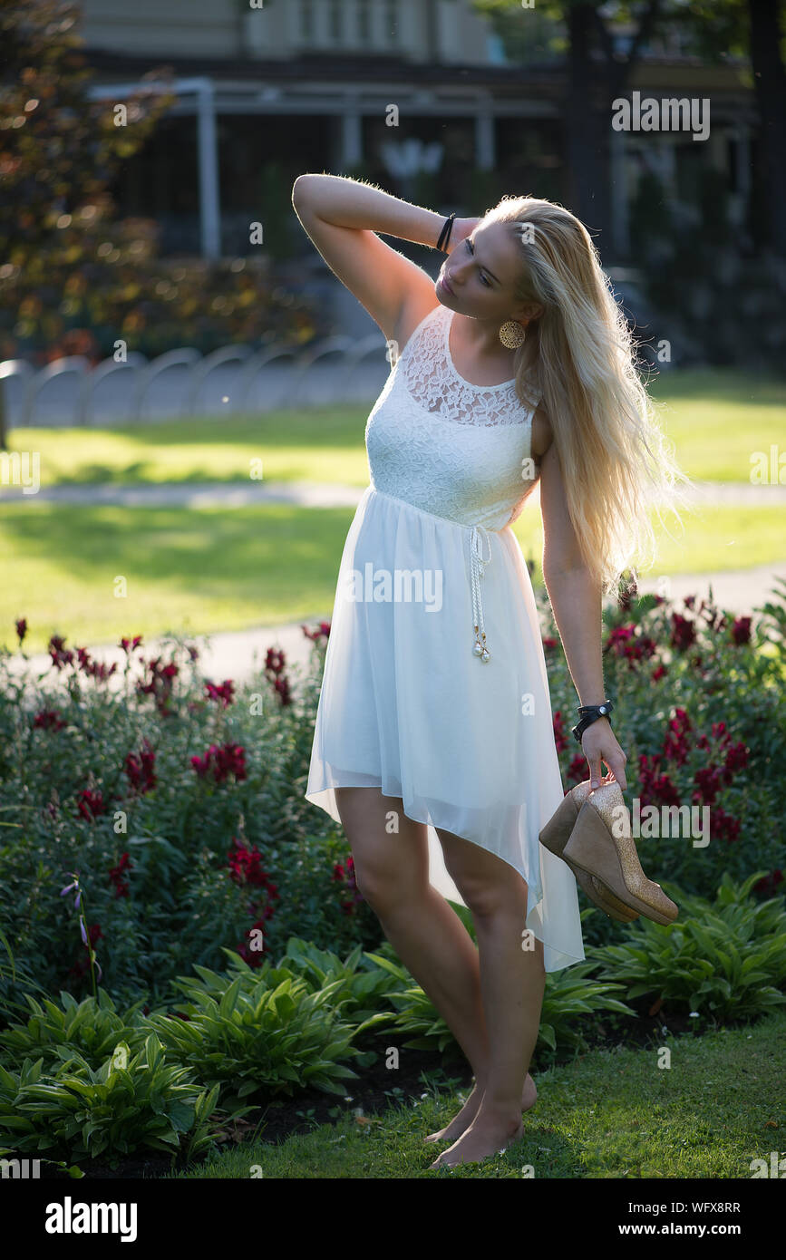 Hermosa Mujer sosteniendo los tacones altos mientras está de pie sobre el  césped en el parque Fotografía de stock - Alamy