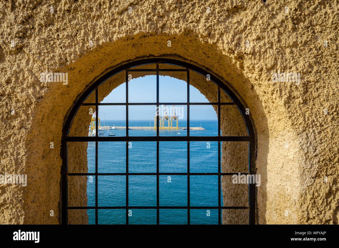 Vista al mar y el puerto a través de una puerta fortificada con barras de hierro desde las alturas de Muttrah Fort. De Muscat, Omán. Foto de stock