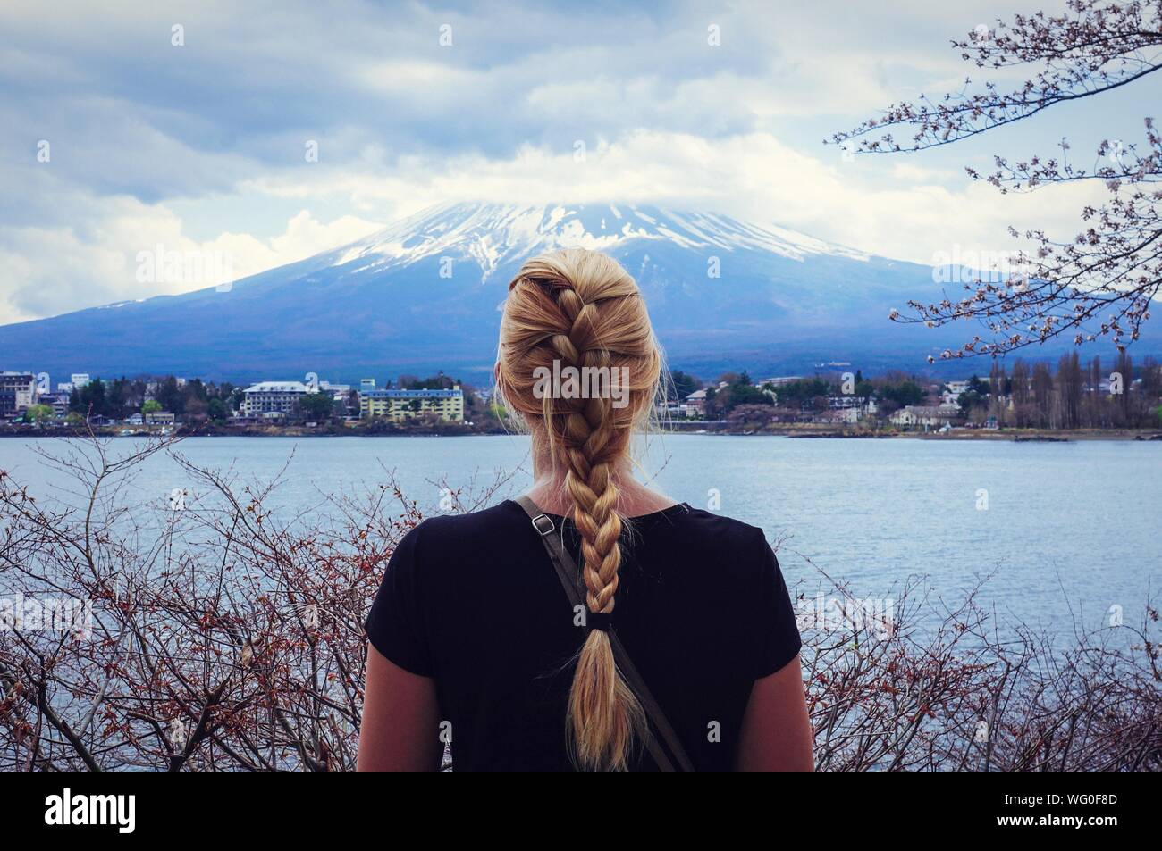 Vista trasera de una mujer con cabello rubio trenzado delante del monte Fuji y el río Foto de stock