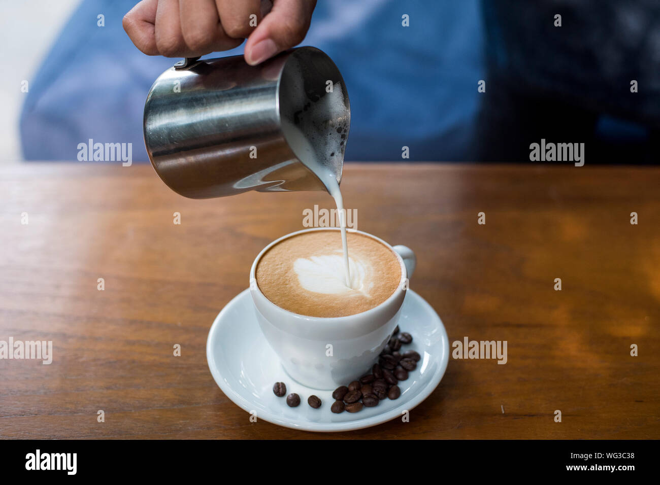 Close-up de mano verter la leche en el café en la mesa Foto de stock