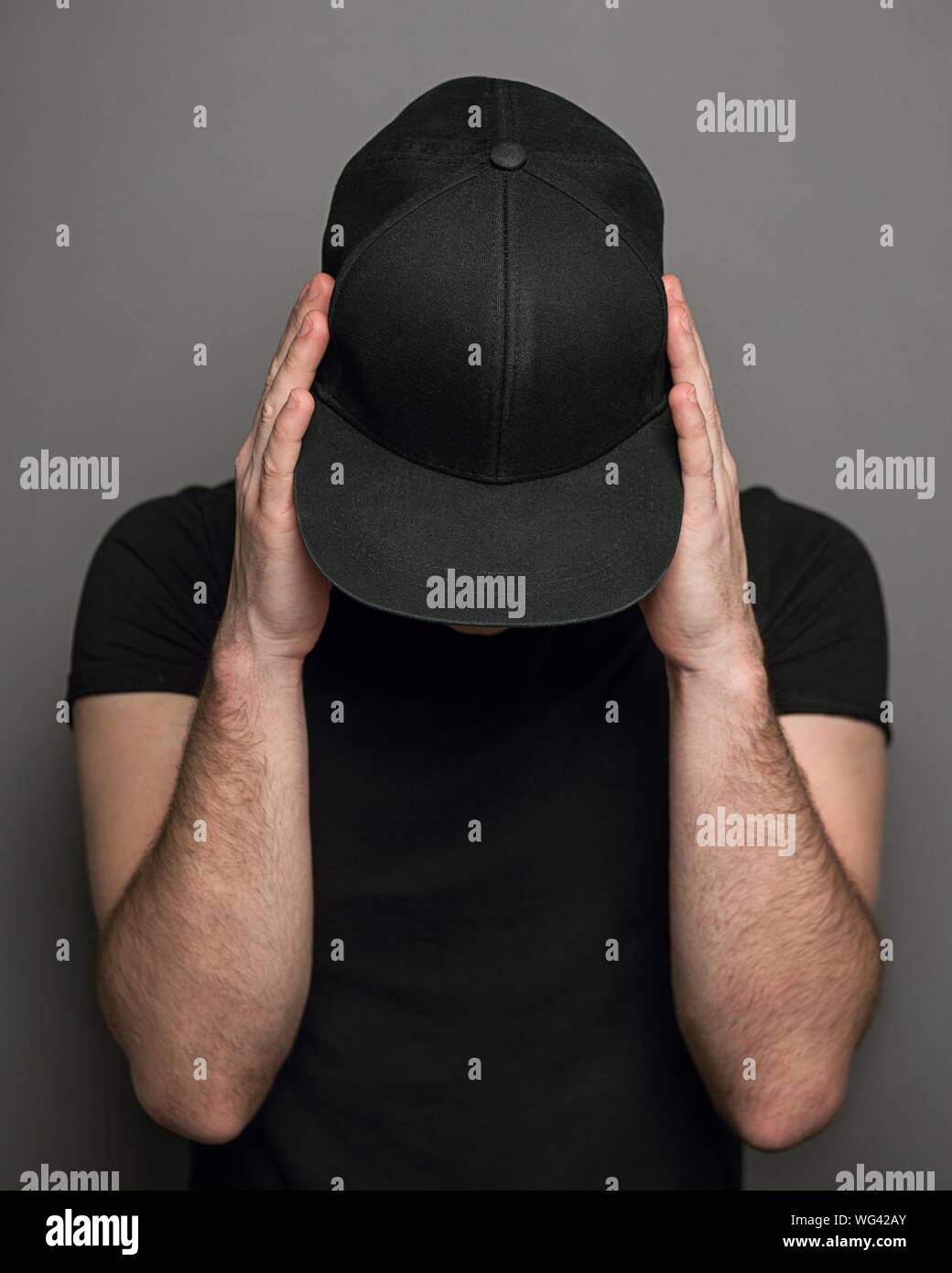Hombre vestido con gorro negro y T-shirt contra un fondo gris Foto de stock