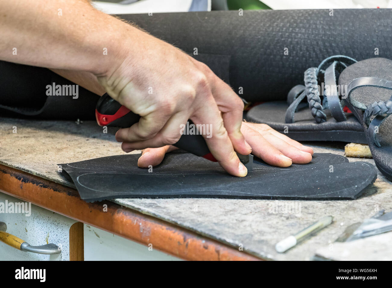 Un hombre zapatero corte manual con un cortador en una suela de goma para  reparar una sandalia Fotografía de stock - Alamy
