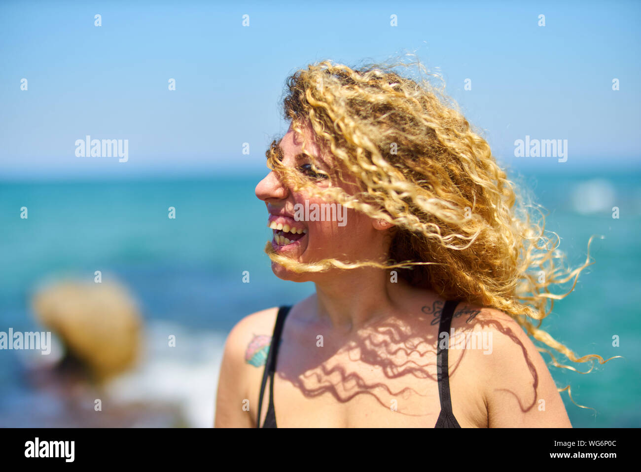 Mujer joven con cabello rubio rizado en la playa Foto de stock