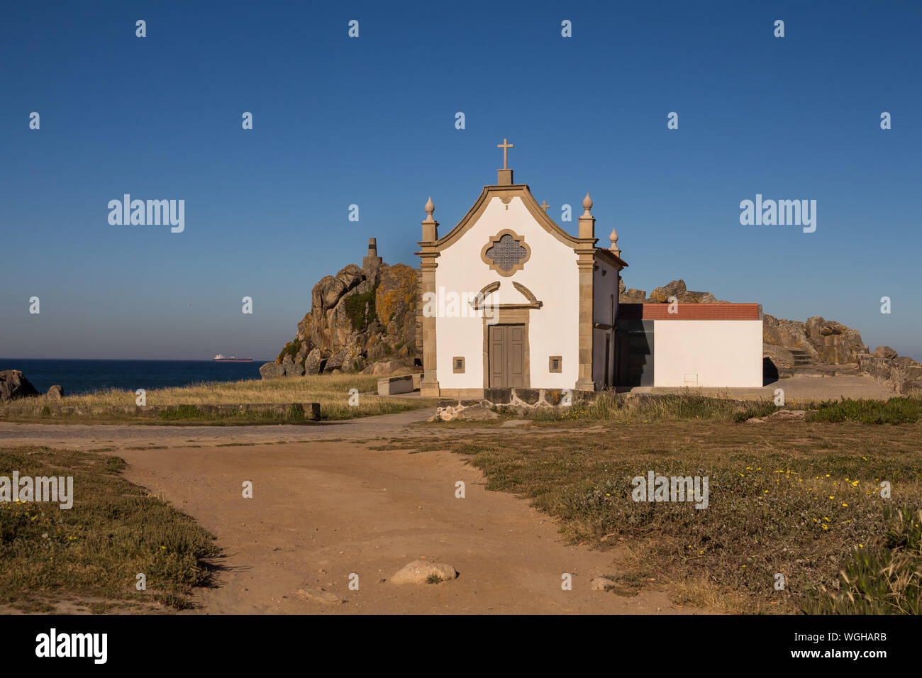 Pequeña capilla blanca construido en estilo tradicional portugués, en la costa del océano Atlántico, junto a una roca. Cielo azul brillante. Porto, Portugal. Foto de stock