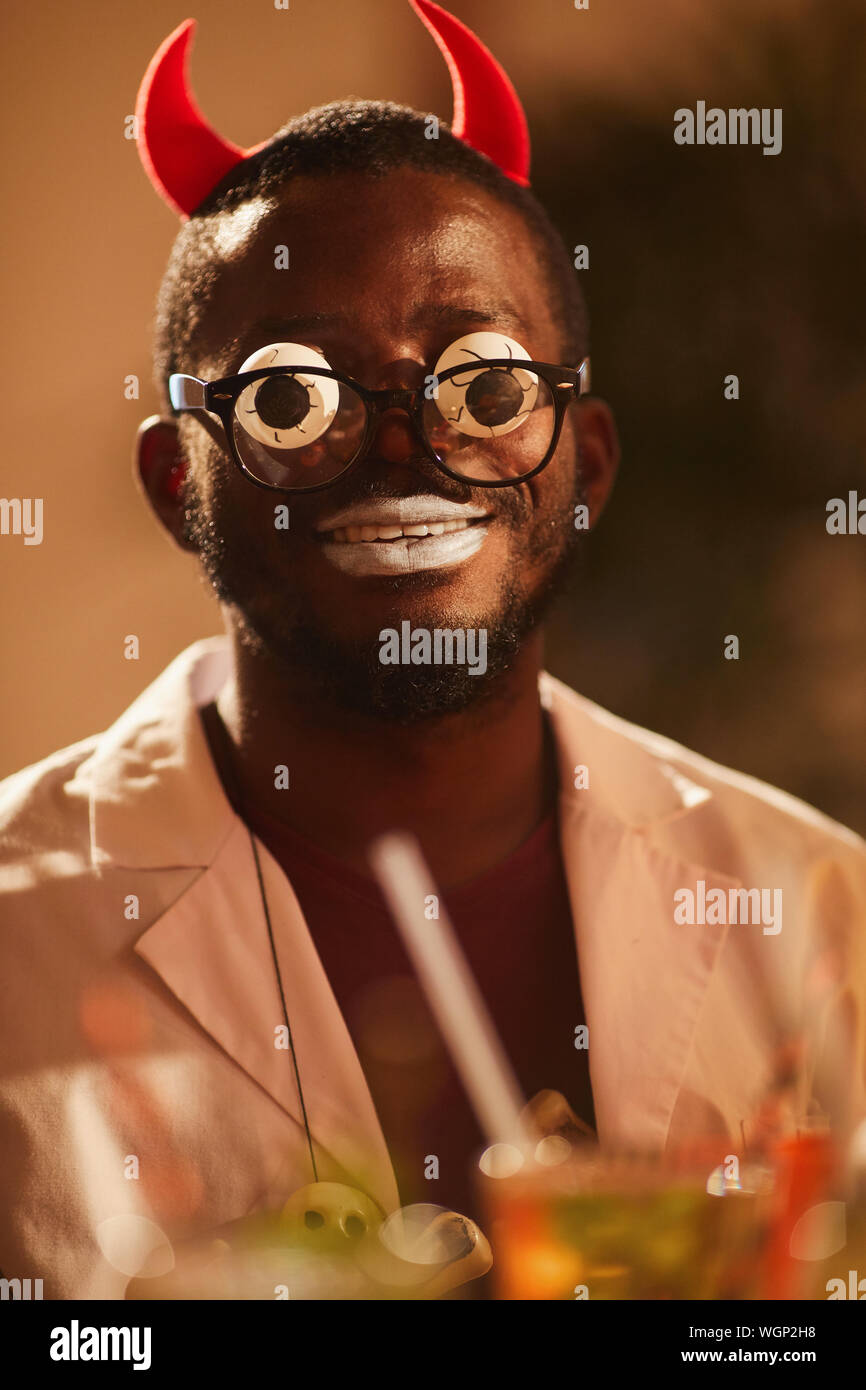 Retrato del hombre africano vistiendo disfraces de Halloween posando como diablo con googly ojos durante la fiesta, espacio de copia Foto de stock