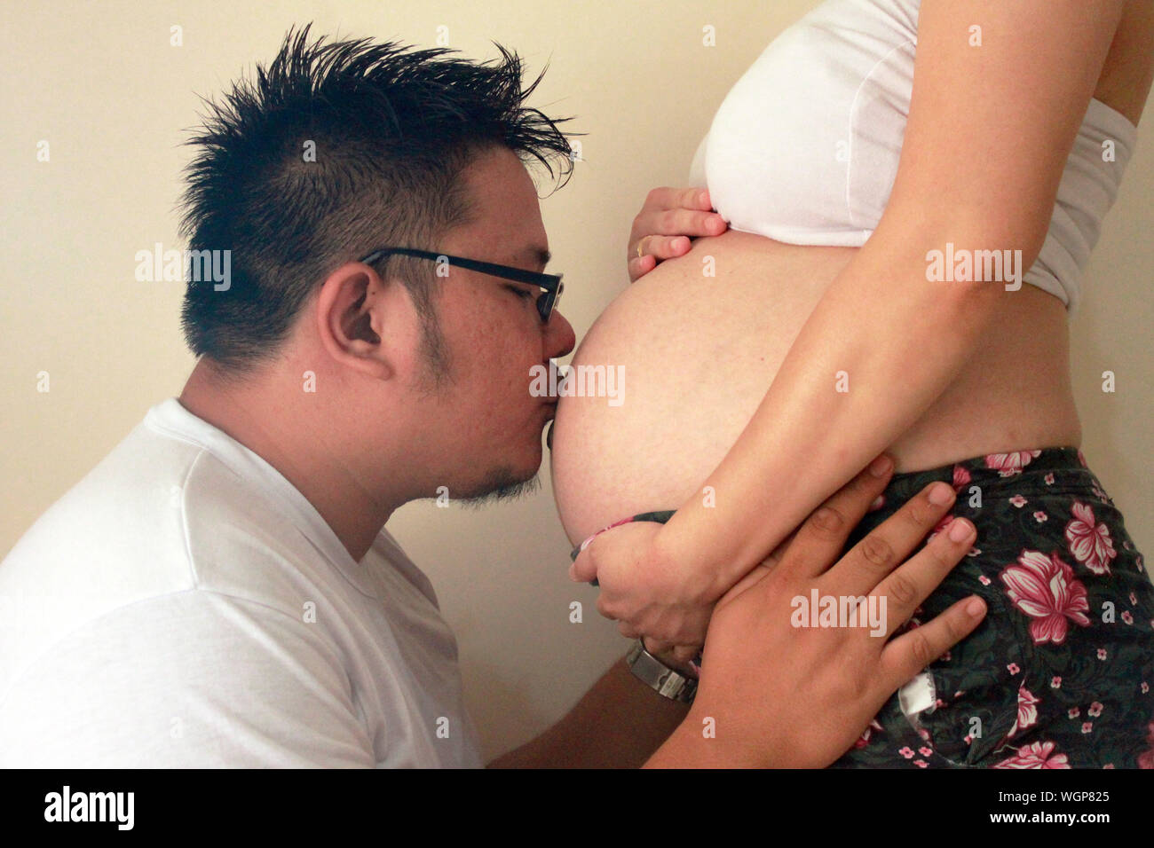 Vista lateral del abdomen de la mujer embarazada besos hombre contra la pared Foto de stock