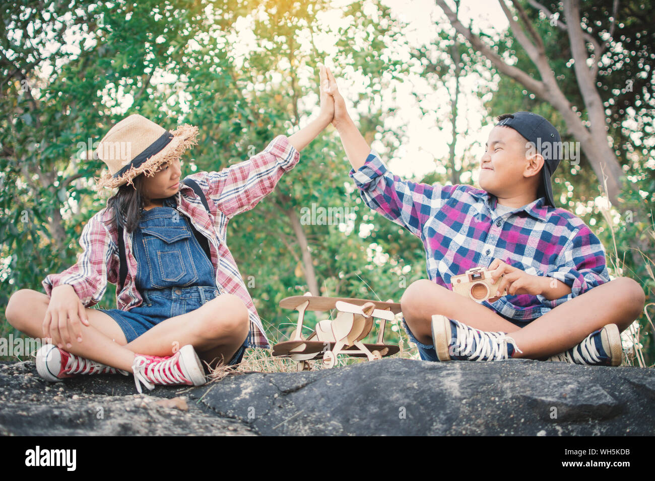 Hermanos haciendo alto cinco mientras sentado sobre una roca en el bosque Foto de stock
