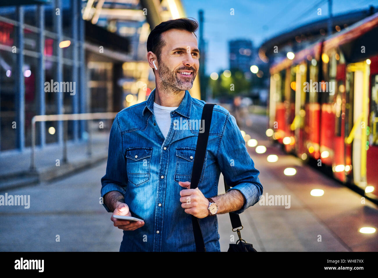 El hombre escucha música mientras espera el tranvía durante la noche conmutar después del trabajo Foto de stock