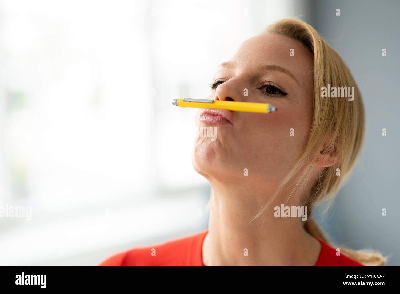 Juguetón joven pluma de equilibrio en su boca en Office Foto de stock
