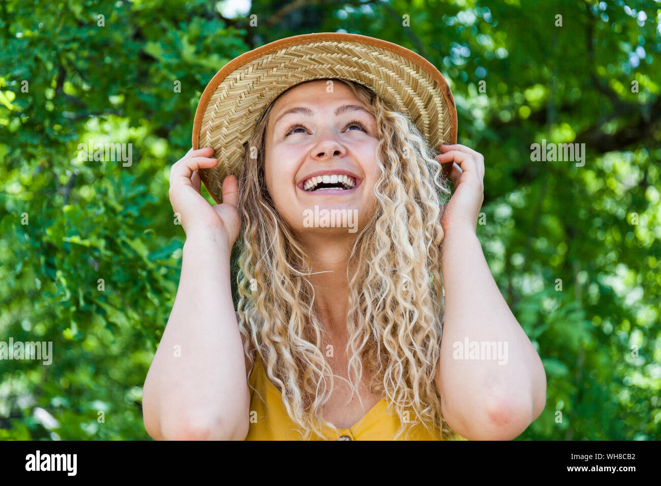 Retrato de mujer rubia sonriente luciendo sombrero de paja, con las manos en HAT Foto de stock