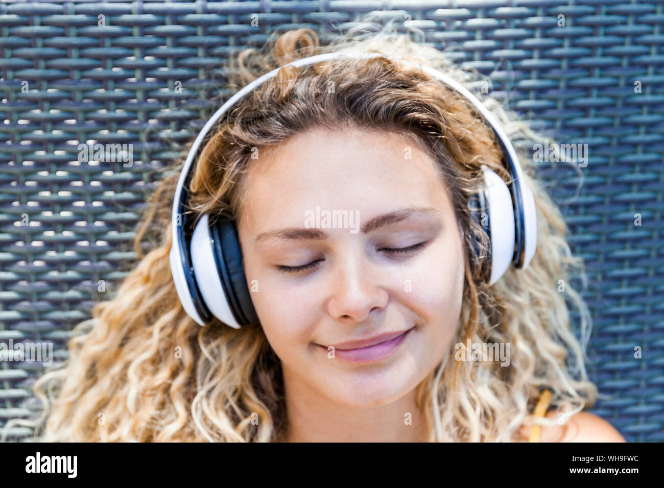 Mujer sonriente al escuchar música con los ojos cerrados, tumbado en la tumbona. Foto de stock