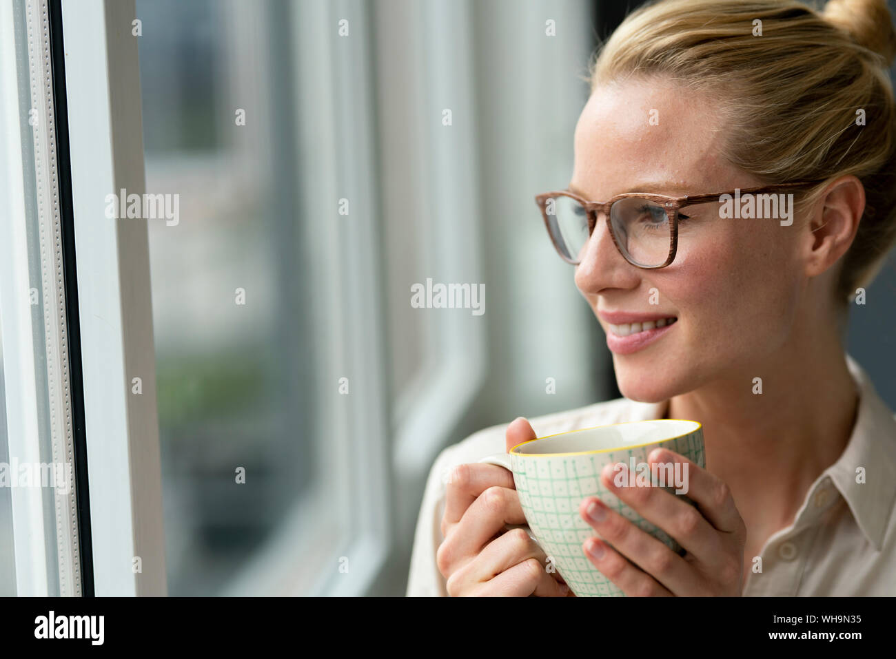 Joven Empresaria con una taza de café mirando hacia afuera de la ventana Foto de stock