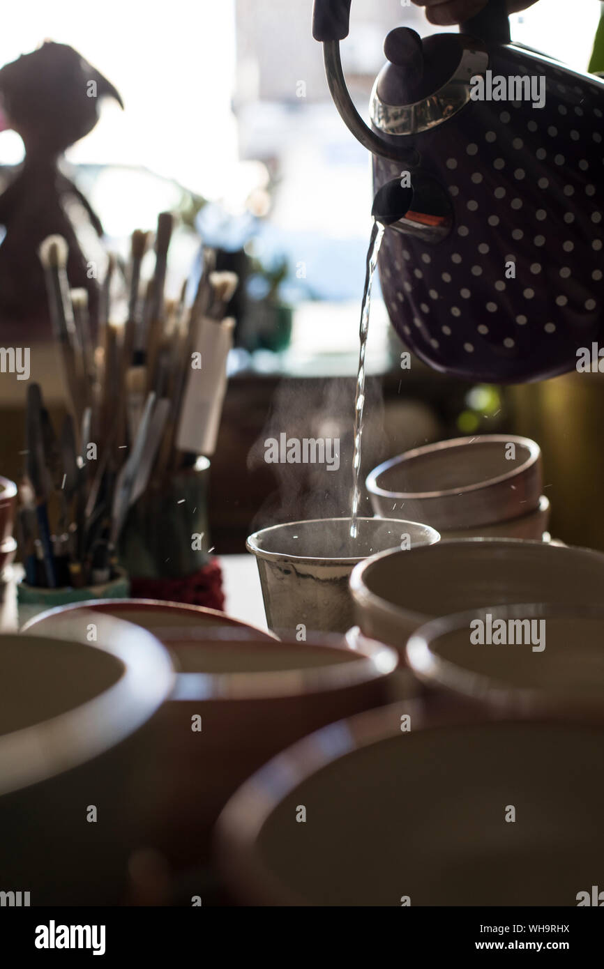 Vertiendo agua caliente en la taza de té en un taller de alfarería Foto de stock