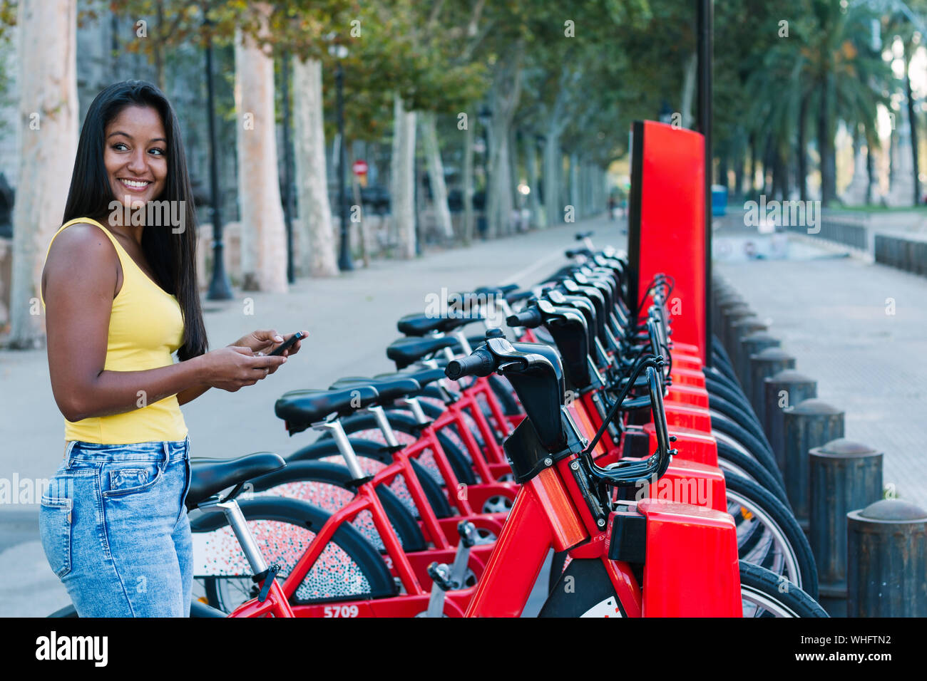 Foto de bella joven controlar su teléfono móvil alquilando una bicicleta en una ciudad Foto de stock