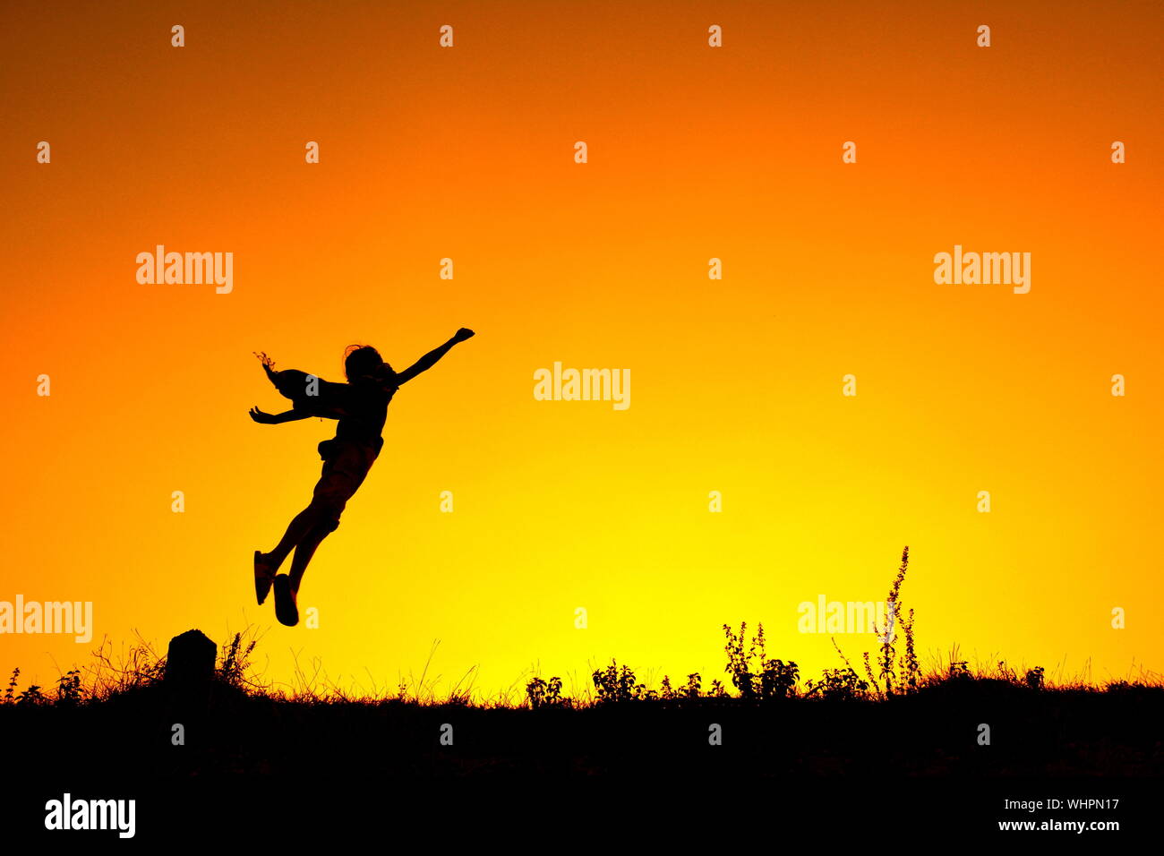Silueta persona saltando en mitad del aire contra el cielo anaranjado Foto de stock