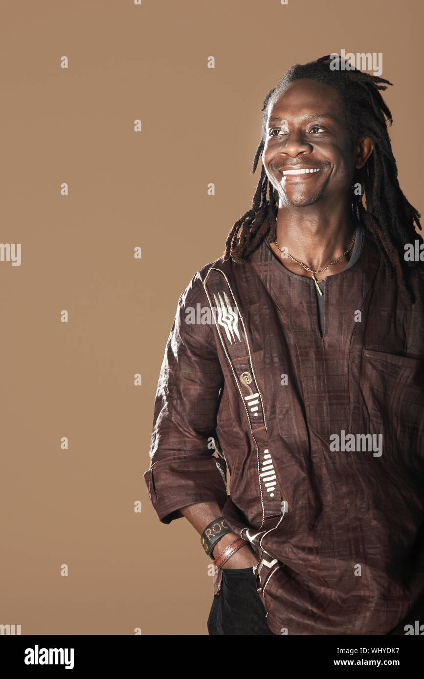 Retrato del hombre afroamericano sonriente con dreadlocks apartar la mirada sobre fondo marrón Foto de stock