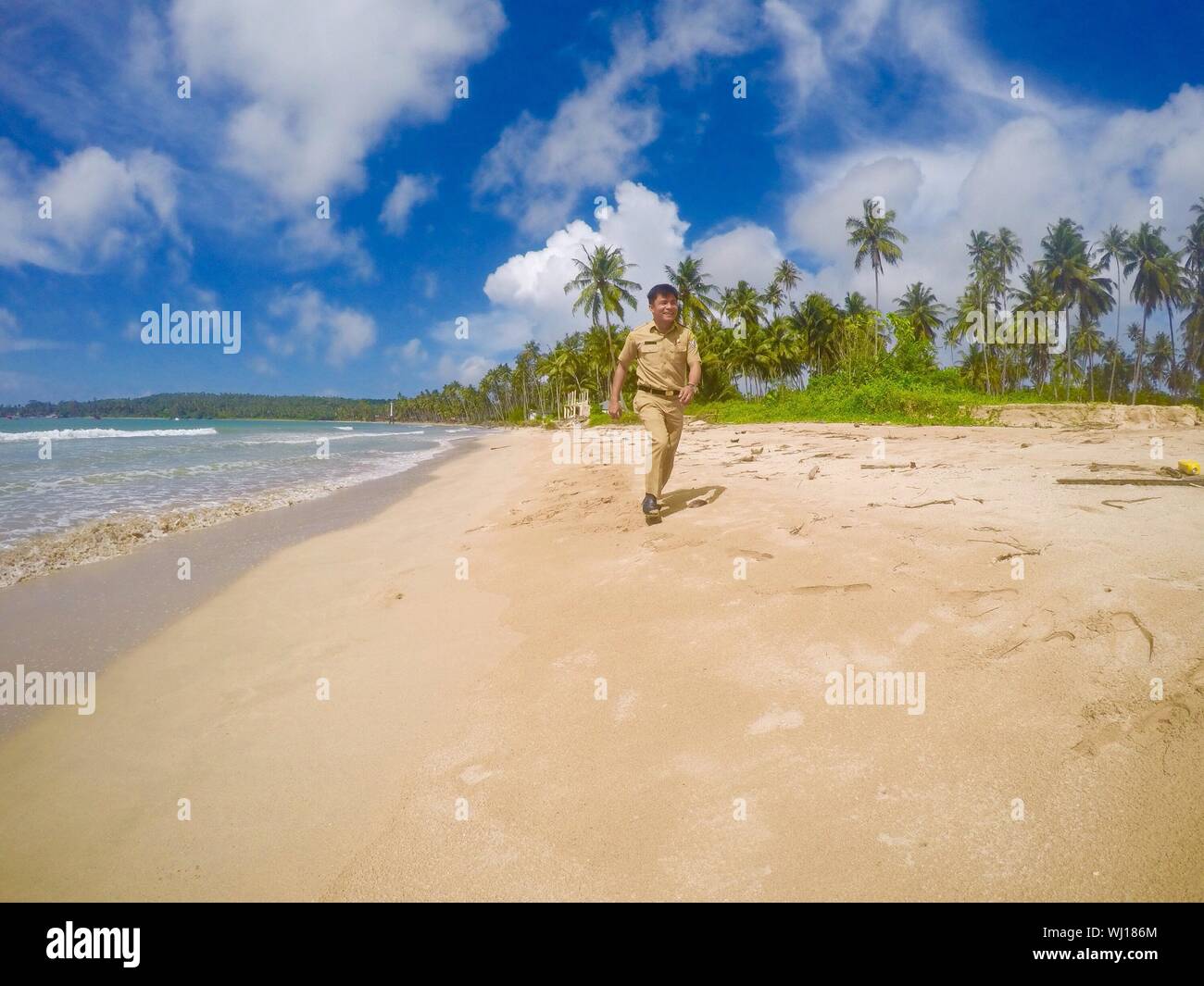 La longitud completa de la policía hombre corriendo en la playa contra el cielo Foto de stock