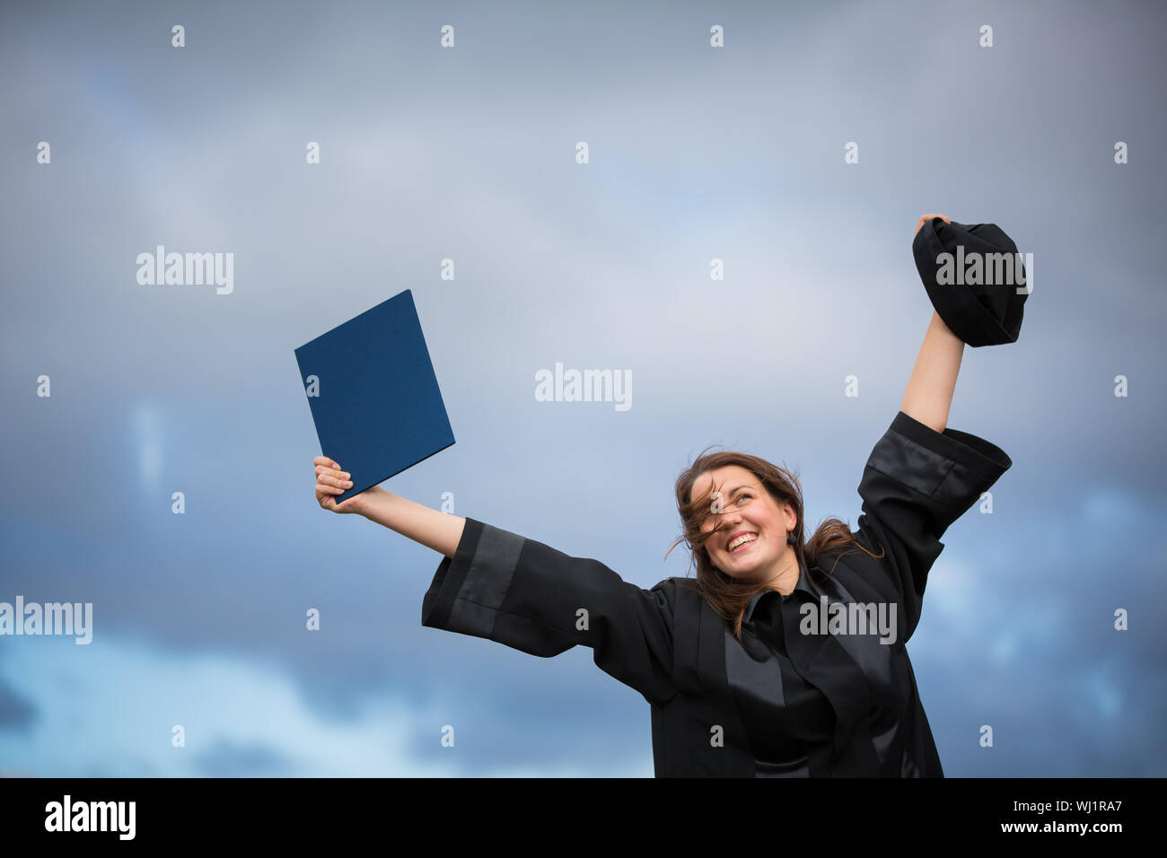 Bastante joven, celebrando con alegría su graduación - difusión amplia sus brazos, sosteniendo su diploma, saboreando su éxito (la imagen en tonos de color; shal Foto de stock