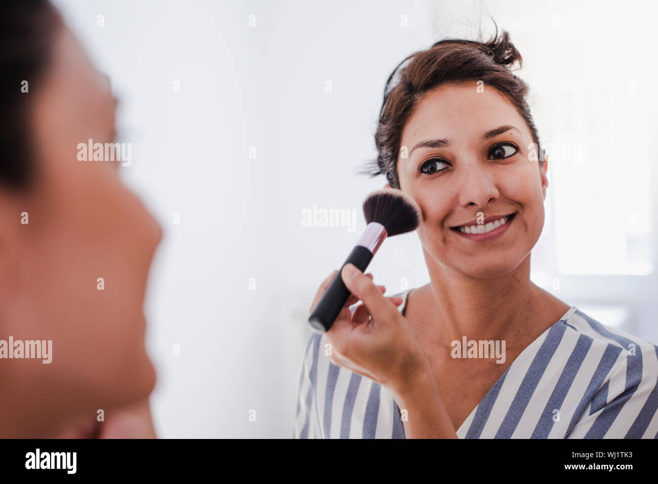 Joven chica latina maquillarse frente al espejo de aplicar la base de maquillaje con una brocha. Foto de stock