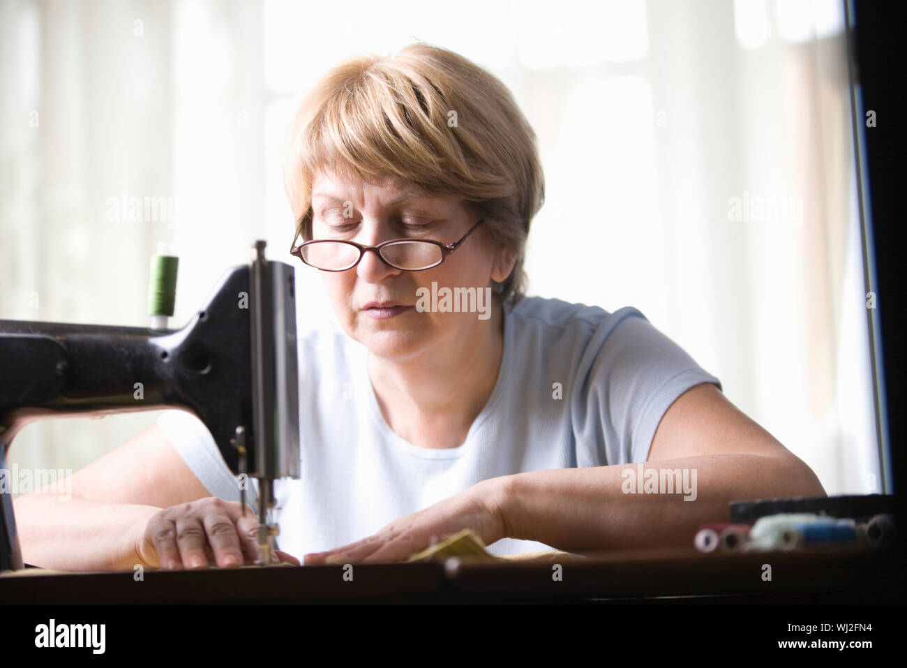 Mujer de más edad con máquina de coser en casa Foto de stock