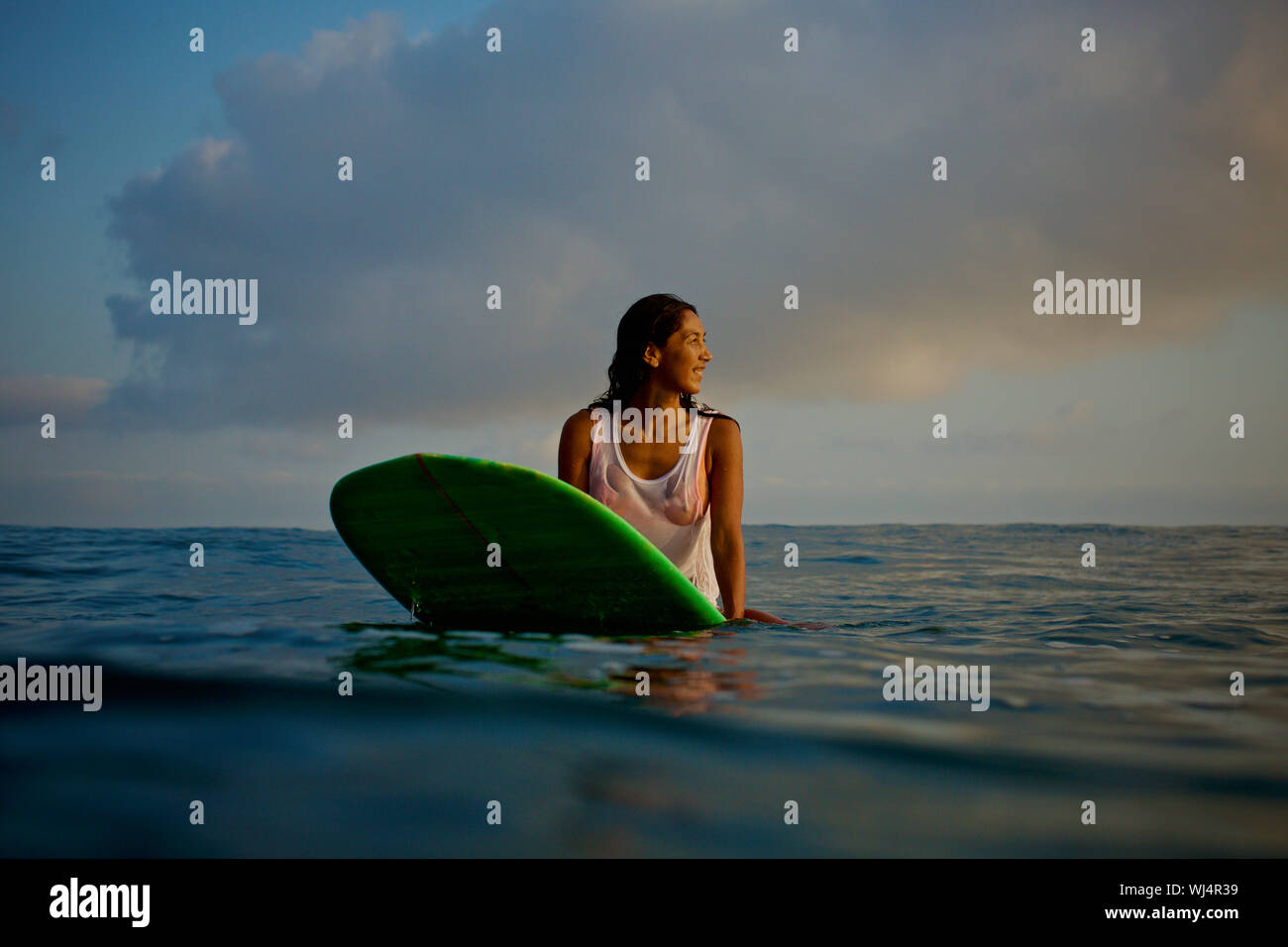Surfer femenina esperando en tablas de surf en el océano Foto de stock
