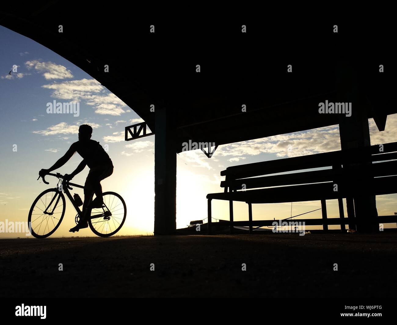 Silueta montando bicicleta en la playa ciclista contra el cielo durante la puesta de sol Foto de stock