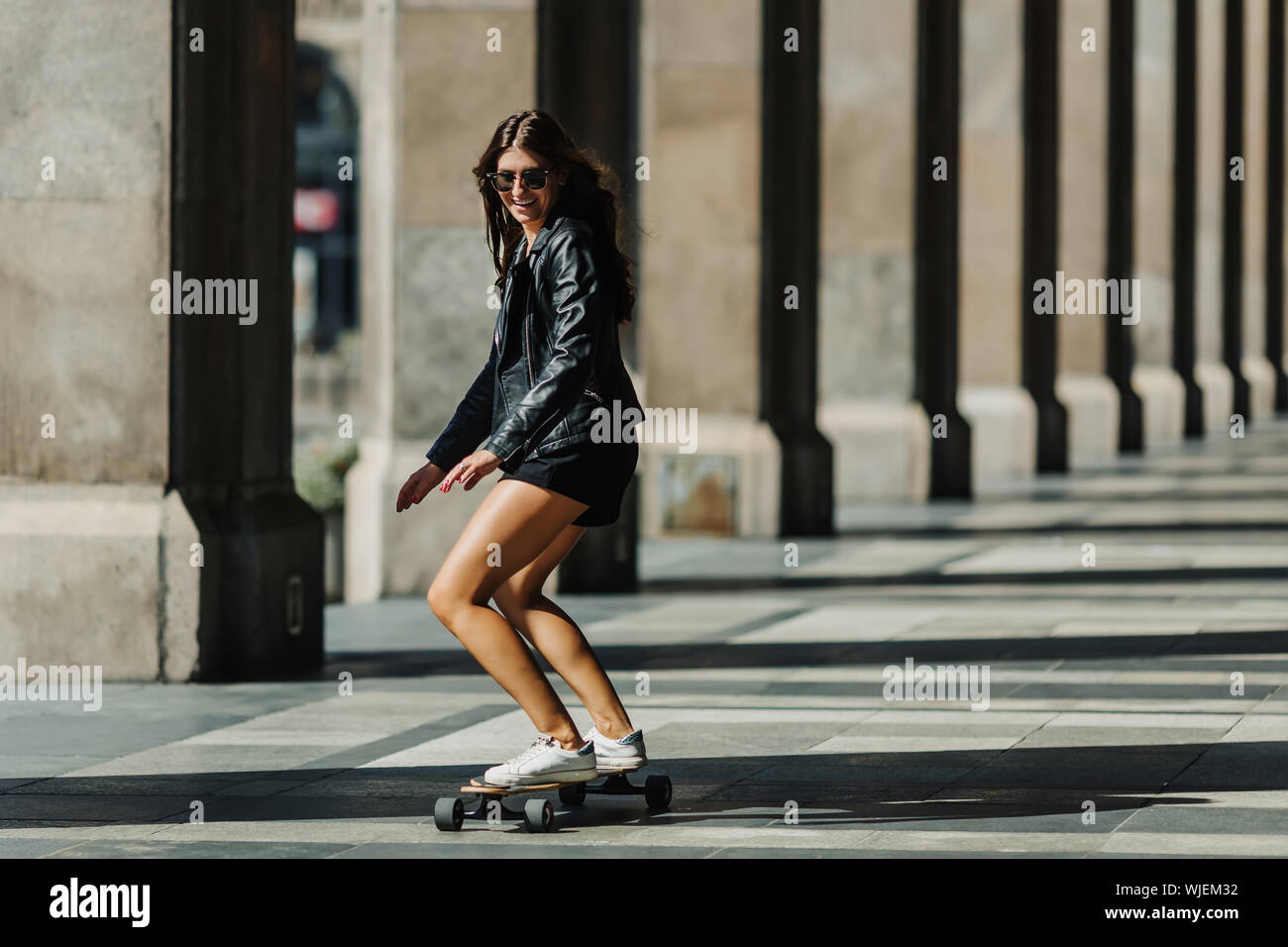 Hermosa mujer joven patinador cabalgando sobre su longboard en la ciudad.  Chica elegante en ropa de calle, paseos en un longboard. Monopatín, foto de  la calle, la vida Fotografía de stock -